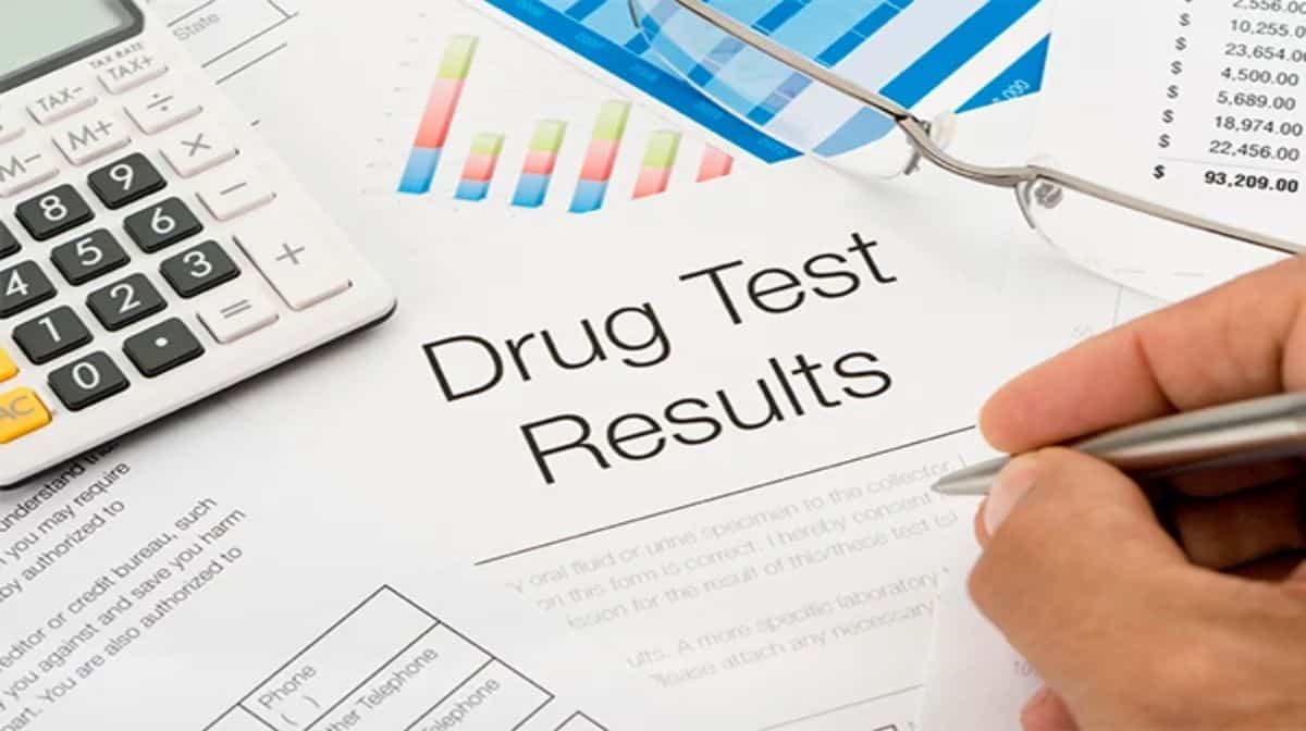 A hand holding a pen on top of the drug test results document. 